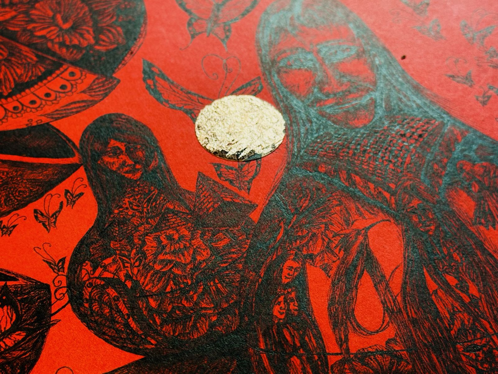 Detail: a gold leaf disc among ink figures on red paper