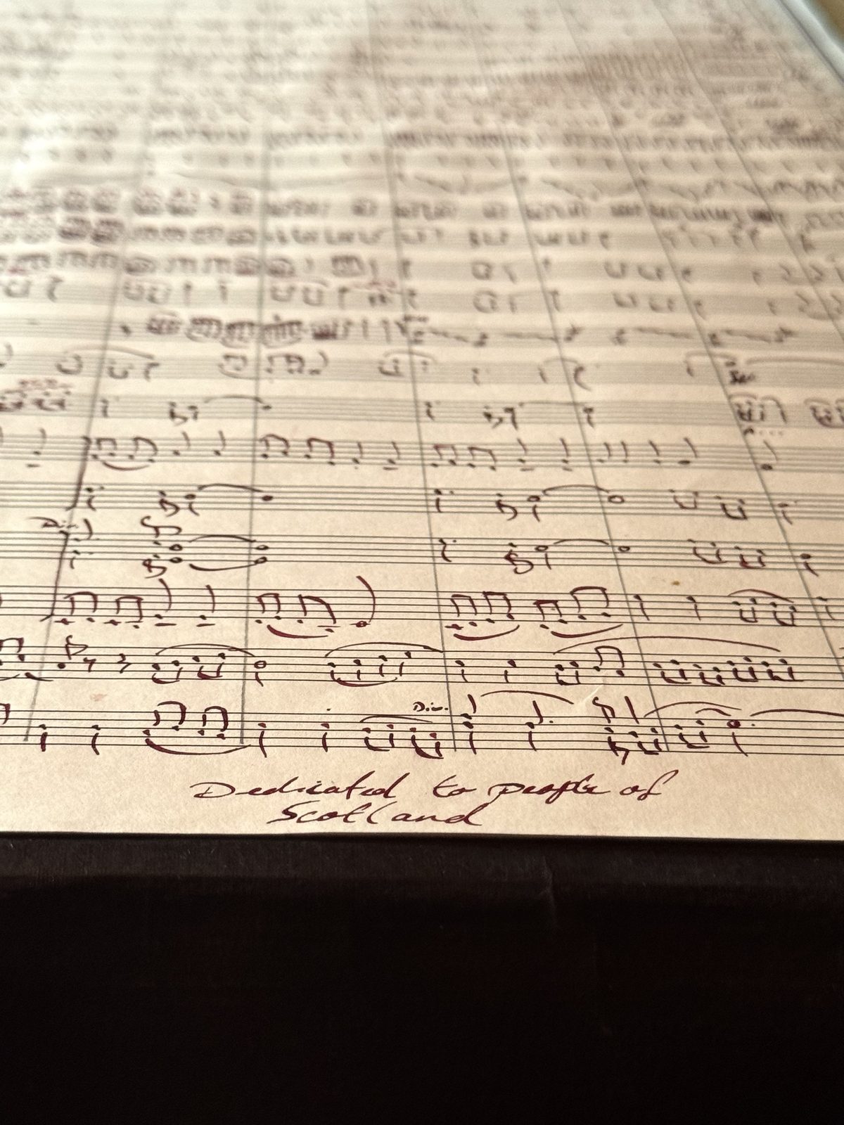 Hand-written orchestral manuscript in burgundy ink, with the dedication to the people of Scotland written beneath the final system