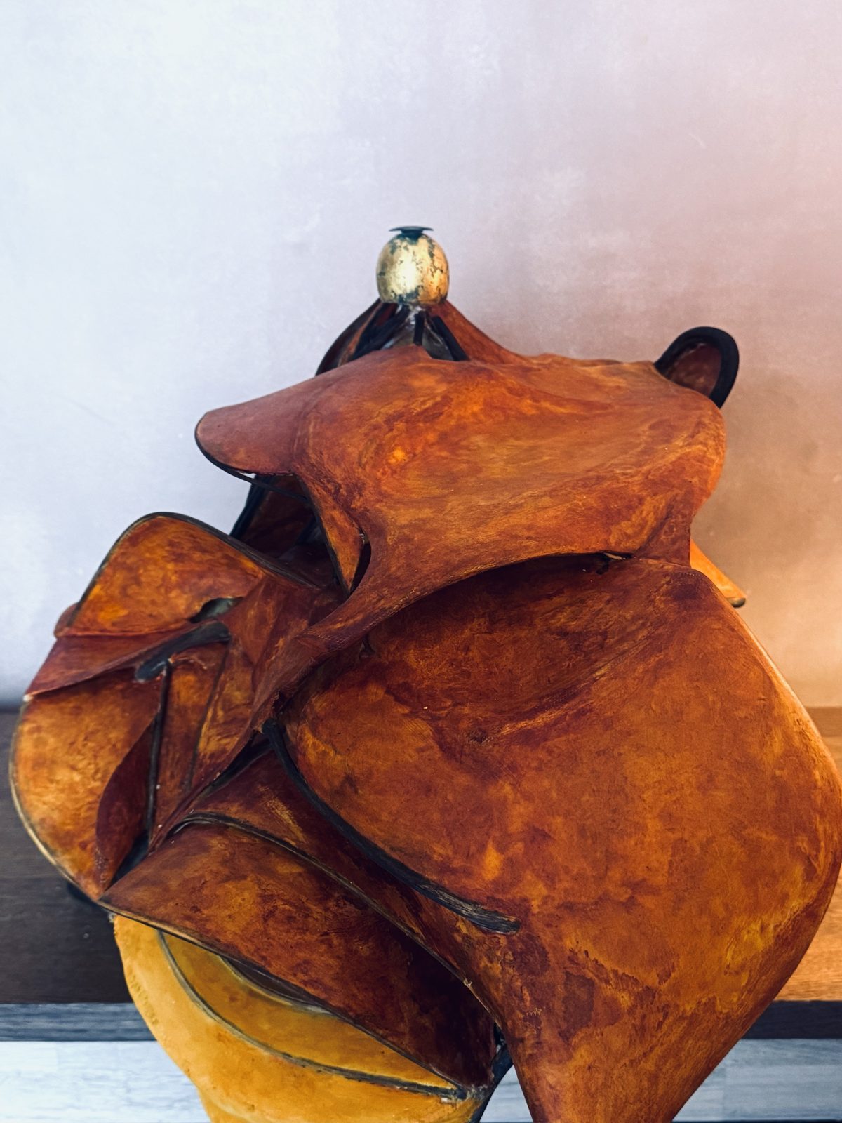 Sculpture of carved and sanded plaster in rust and ochre tones, folding like petals and wings in flowing, aerodynamic curves, topped with a small gilded egg