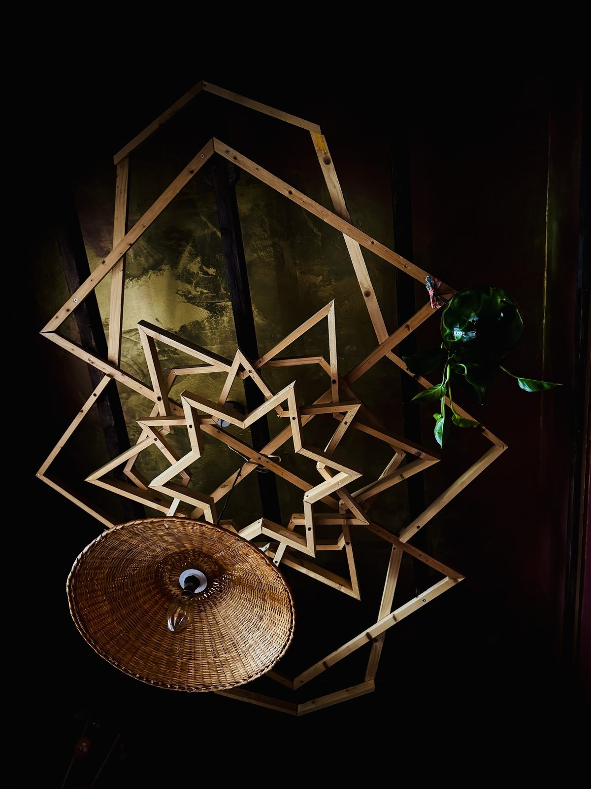The wooden star structure seen from below, with a woven cane lampshade hanging in front of it